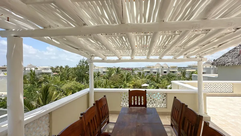 Emanuela Apartment's rooftop terrace under a white pergola, with a dining table and a treetop view