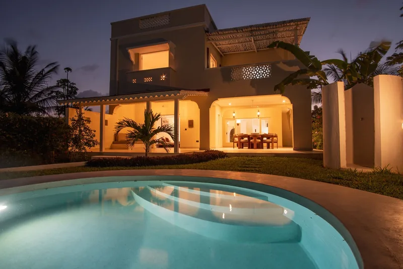 The Usalu Villa's exterior at dusk, with a lit interior and the pool in front